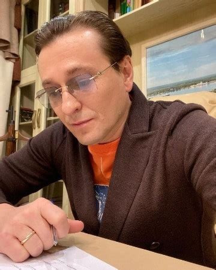Sergey Bezrukov posing for a photo by wearing orange vest and brown cloth.